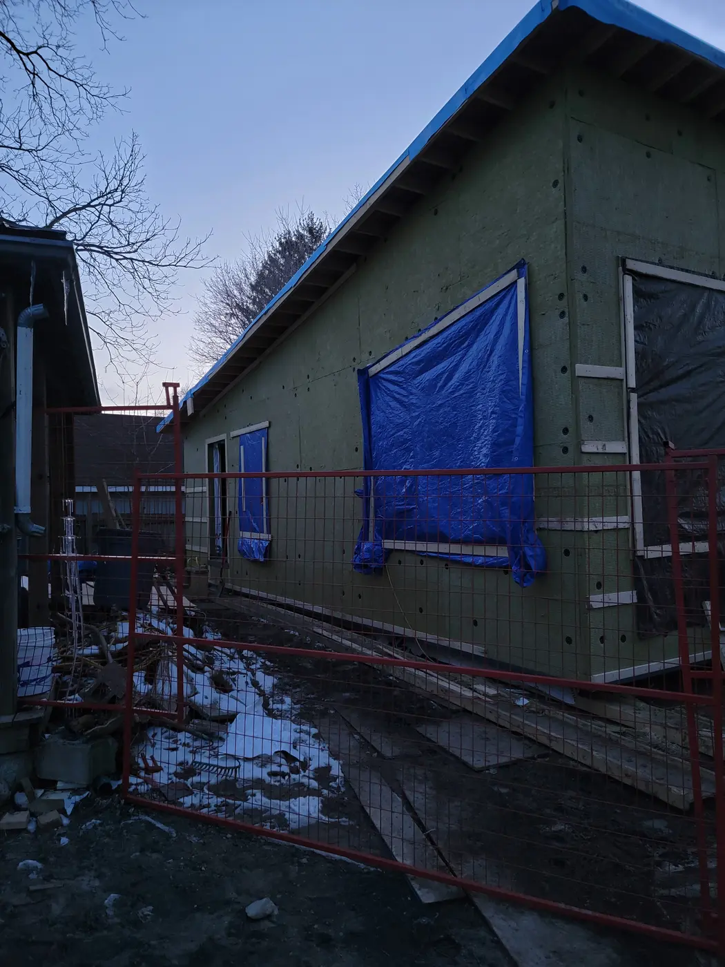 Exterior of the garden suite wrapped in green Rockwool Comfort Board continuous insulation, with windows temporarily protected by tarps