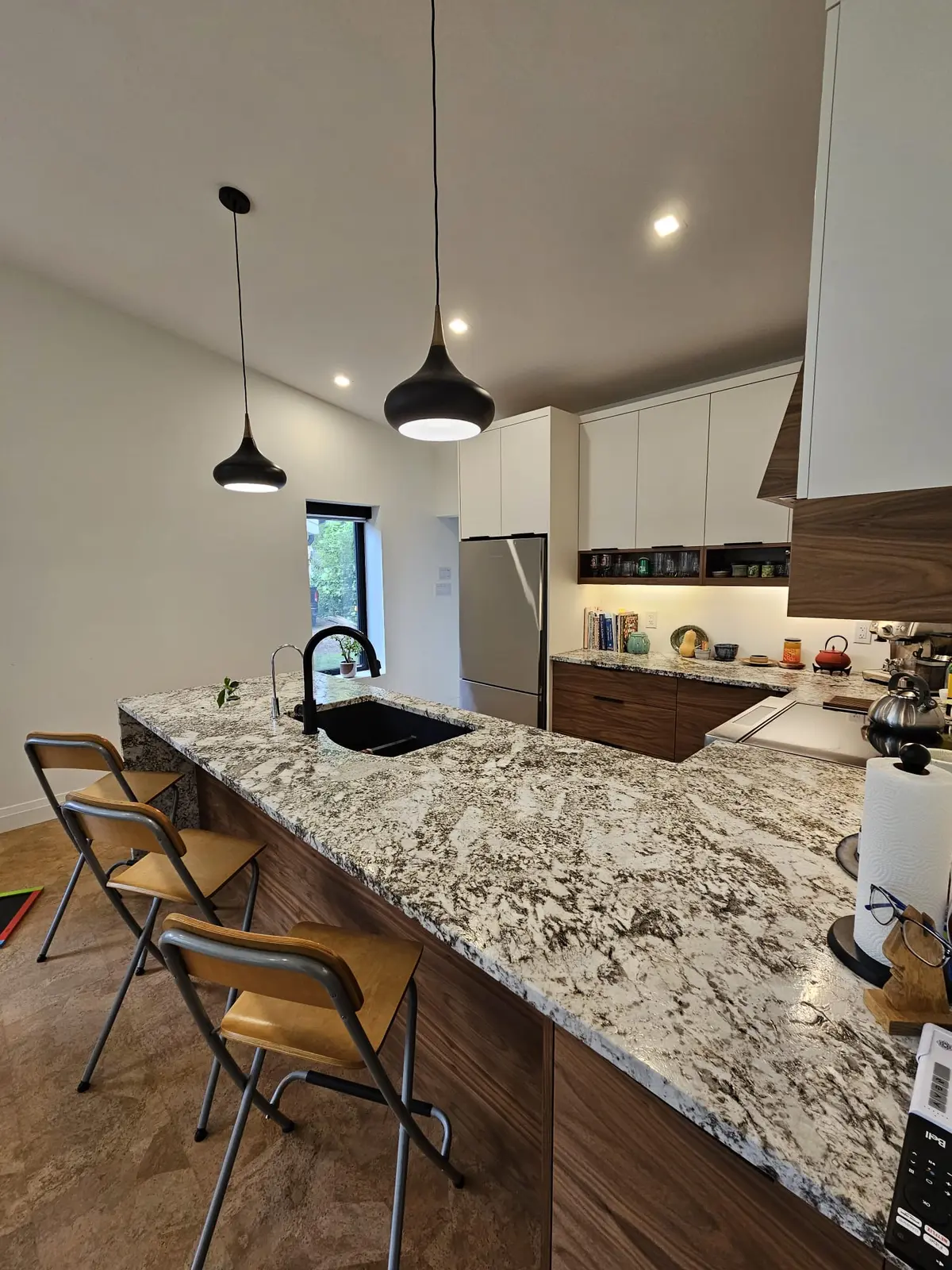 Finished kitchen with white and walnut flat-panel cabinetry, a granite peninsula, black pendant lights, and a walnut range hood