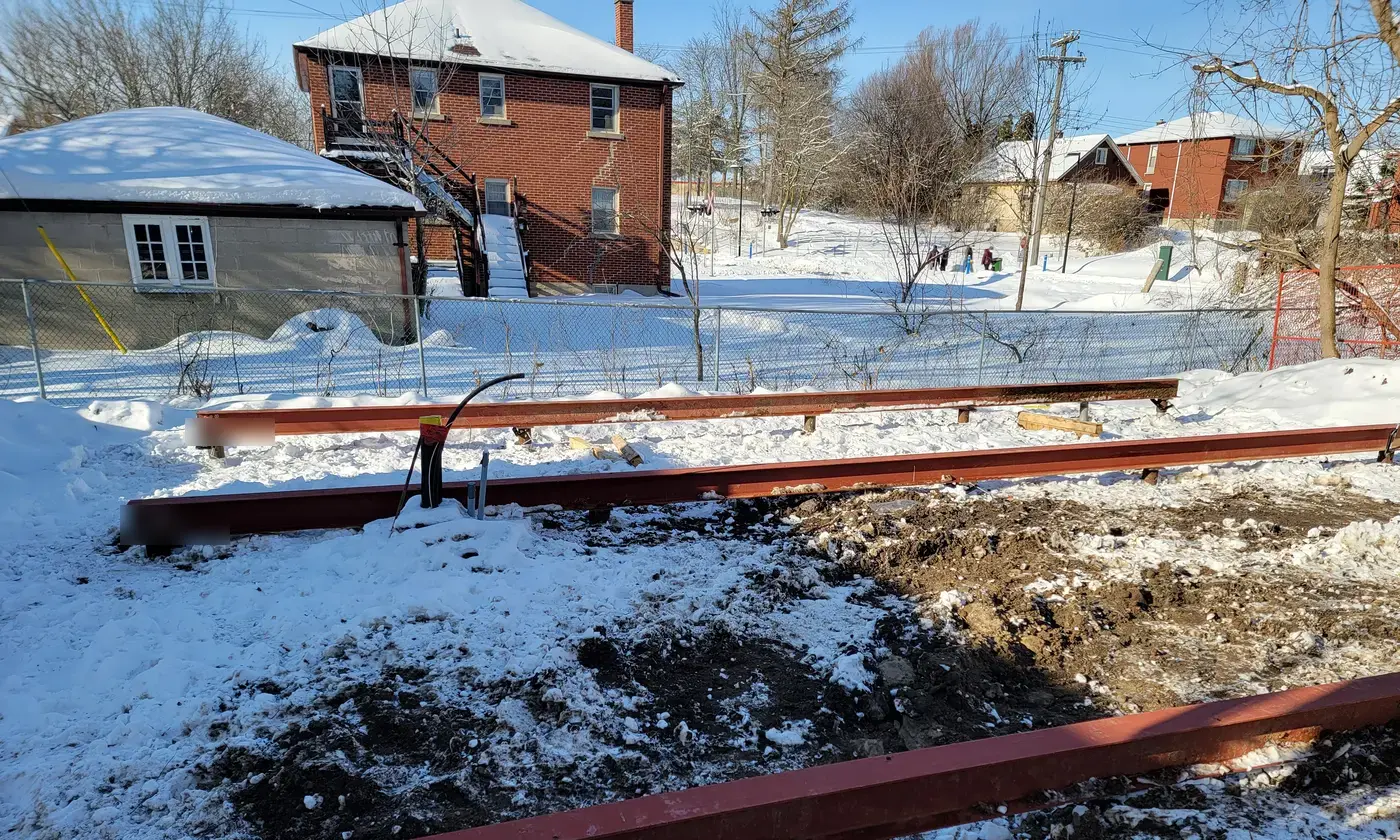 Red structural steel beams laid across the snowy lot, forming the support grid for the floor system